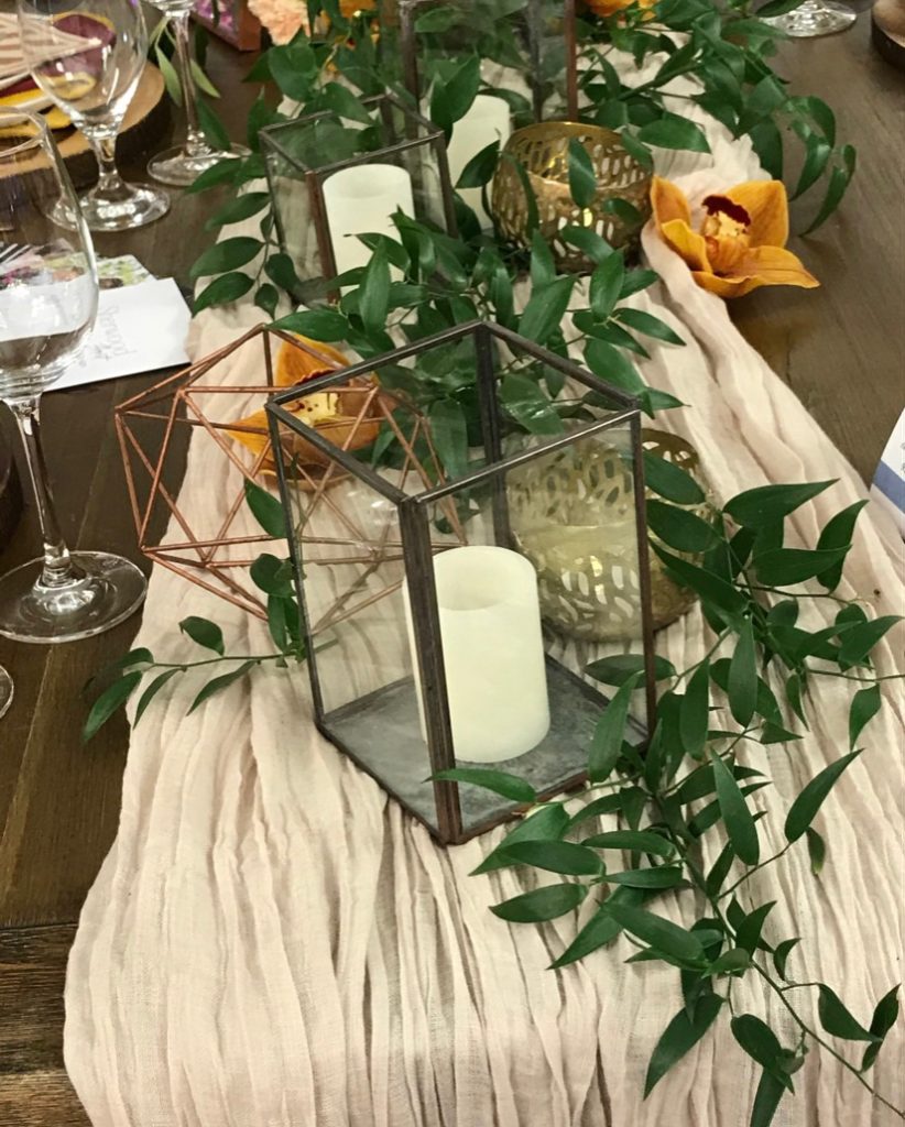 Table runner with ruscus, lanterns, and candles - along with a few gold felt flowers - is eco-friendly
